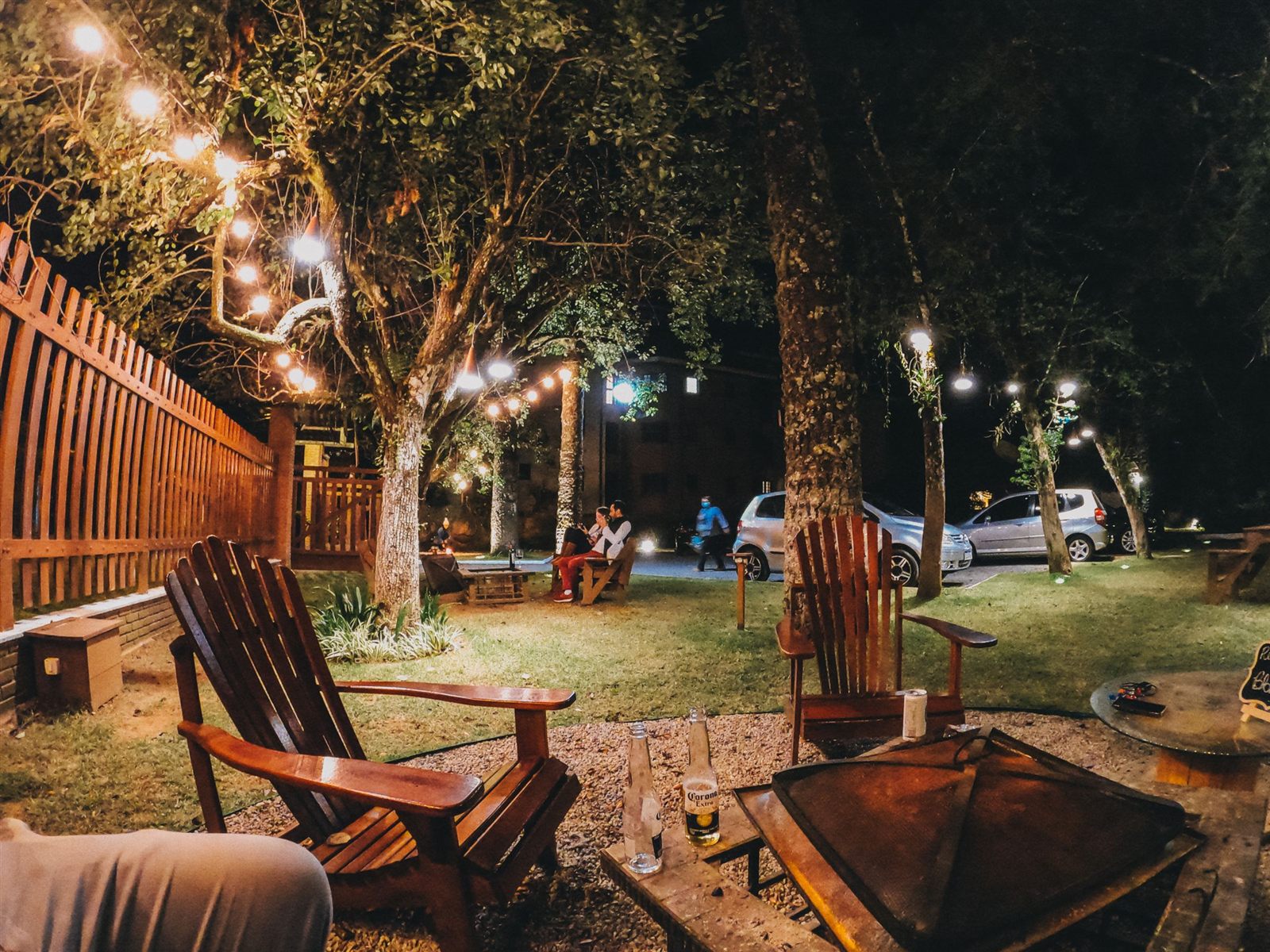 A backyard at night glowing with string lights, wooden lounge chairs and a fire pit