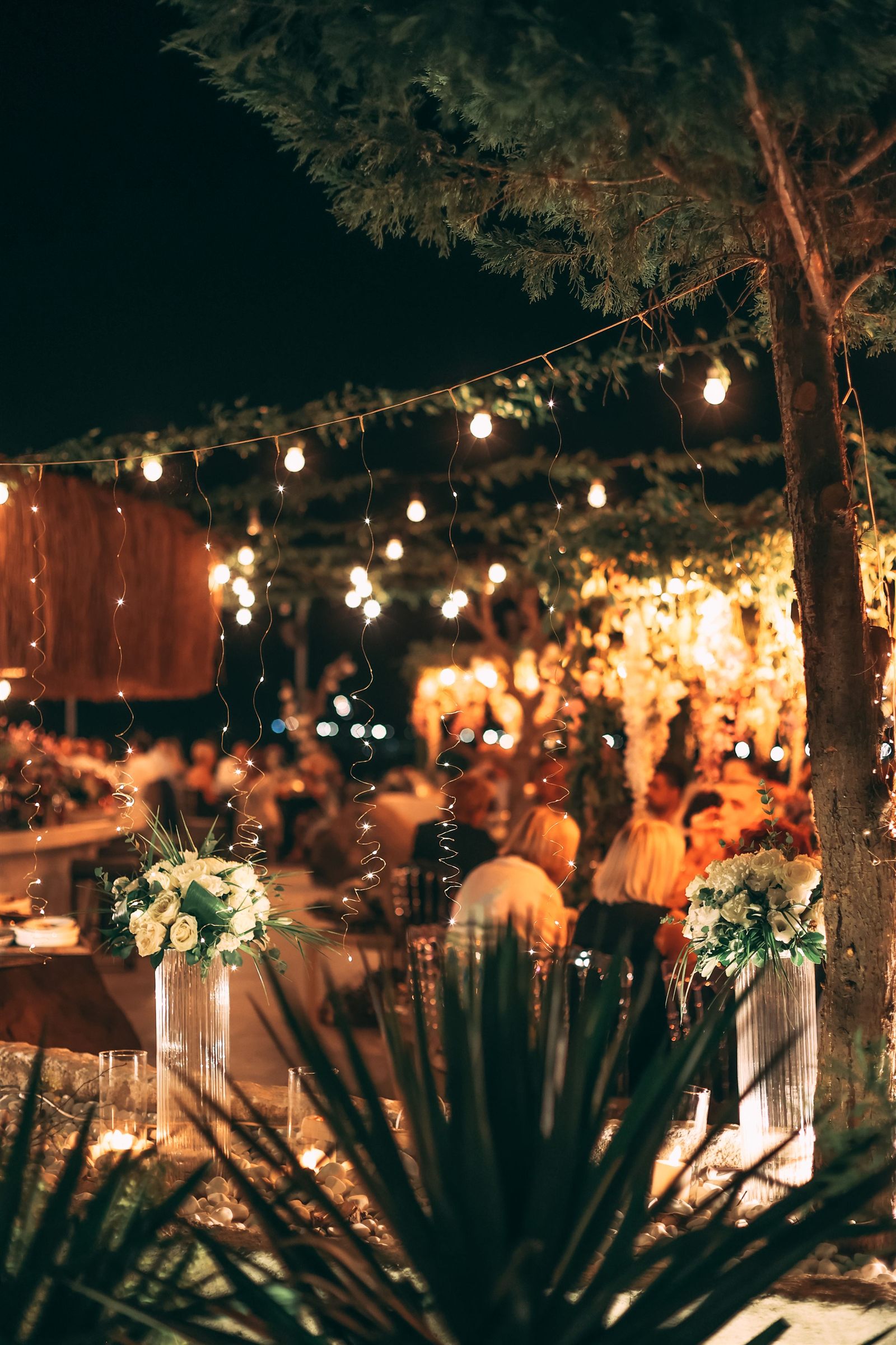 An outdoor evening celebration glowing with string lights and flowers